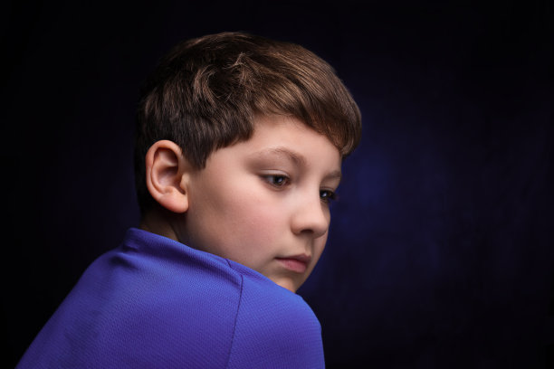 侧面沉思的高加索少年男孩与浅棕色的头发和刘海，穿着运动紫色t恤在孤立的背景图片下载