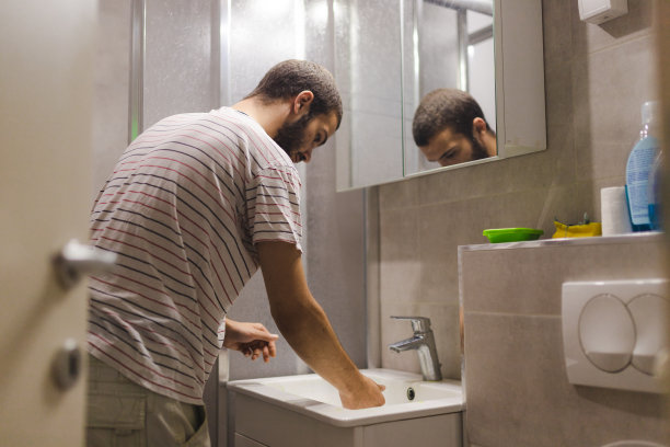 一个年轻人在他的公寓里用抹布清洁浴室的水槽/水龙头图片下载