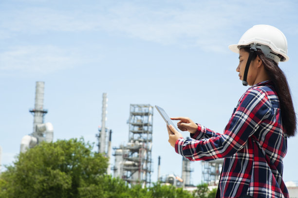 亚洲电气女工程师在电厂电站穿着安全防护服，戴安全帽，站着检查和处理技术问题，用平板记录测量结果。图片下载