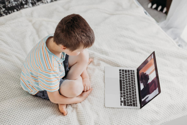 在家远程学习。男生坐在床上，用数字平板电脑看网络研讨会图片下载