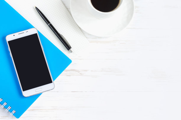 笔记本，笔，眼镜，手机，白色木桌上的一杯咖啡，平放，俯视图。办公桌办公桌，工作场所图片下载