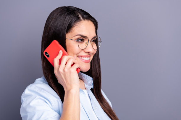 照片中迷人甜美的成熟女人穿着正式的衬衫，眼镜说话现代装置孤立的灰色背景图片下载