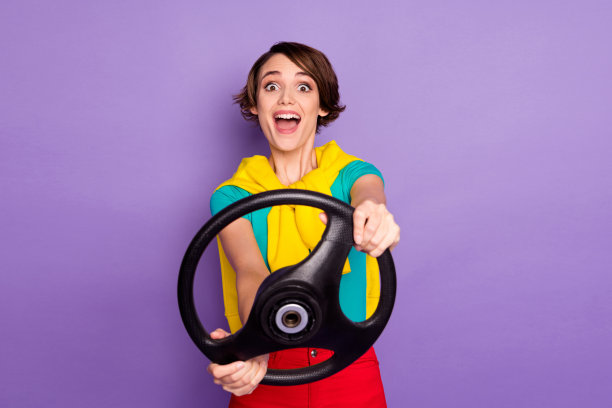 照片中的女孩张开嘴握住方向盘，穿着打结的毛衣t恤，孤立的紫色背景图片下载