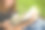 一个穿着牛仔裤的女人端着一杯咖啡坐在公园的毯子上看书图片下载