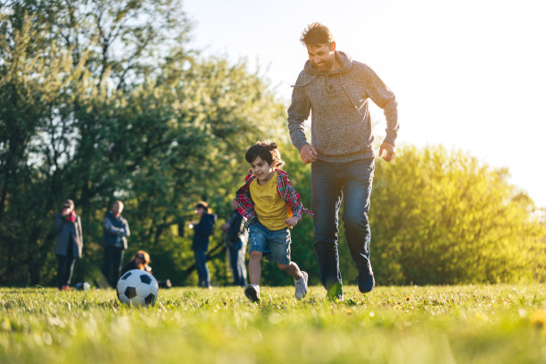 日落时分，男孩和父亲在公园里踢足球图片下载