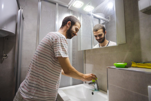 年轻开朗的男子正在用清洁布/抹布和清洁产品清洁浴室的水槽图片下载