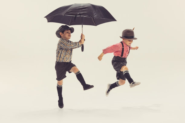 两个活泼的小男孩的肖像，孩子们玩伞，跳跃孤立在灰色的工作室背景图片下载