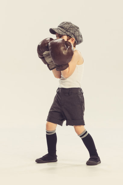 小男孩的肖像，孩子在巨大的拳击手套摆姿势，玩孤立的灰色工作室背景图片下载