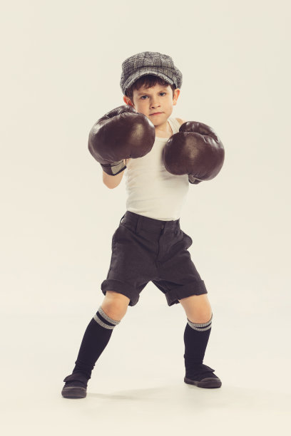 小男孩的肖像，孩子在巨大的拳击手套摆姿势，玩孤立的灰色工作室背景图片下载