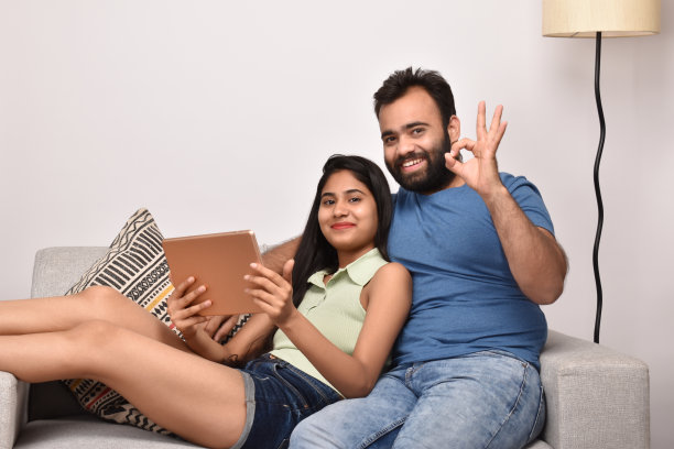 一对年轻的情侣坐在沙发上，用着数码平板电脑图片下载