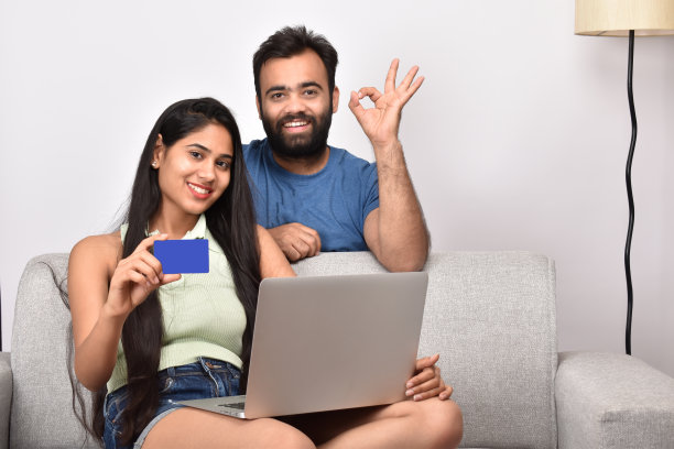 一对年轻夫妇坐在沙发上用笔记本电脑图片下载