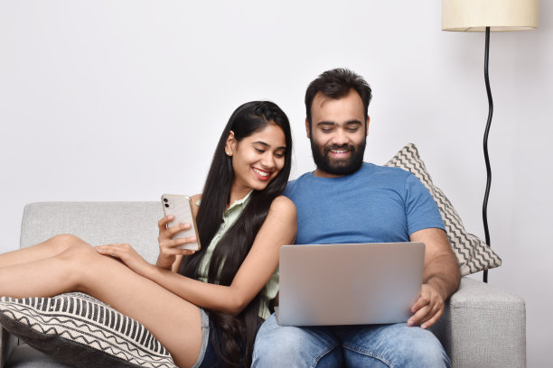 年轻的情侣坐在沙发上，使用智能手机和笔记本电脑图片下载