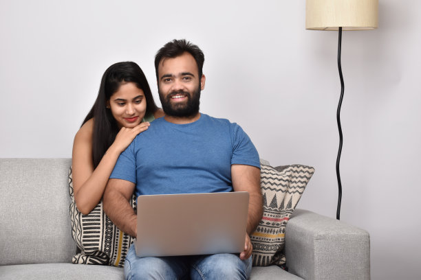 一对年轻夫妇坐在沙发上用笔记本电脑图片下载