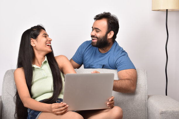 一对年轻夫妇坐在沙发上用笔记本电脑图片下载