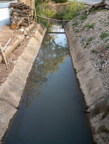 混凝土排水沟在一个农民的房子前面。图片下载