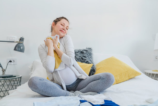 美丽的年轻微笑的孕妇在为她的孩子准备衣服。幸福图片下载