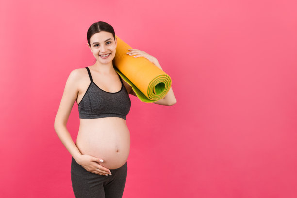 抱着瑜伽垫的怀孕女孩站在彩色背景上。工作室拍摄，设计的自由空间图片下载