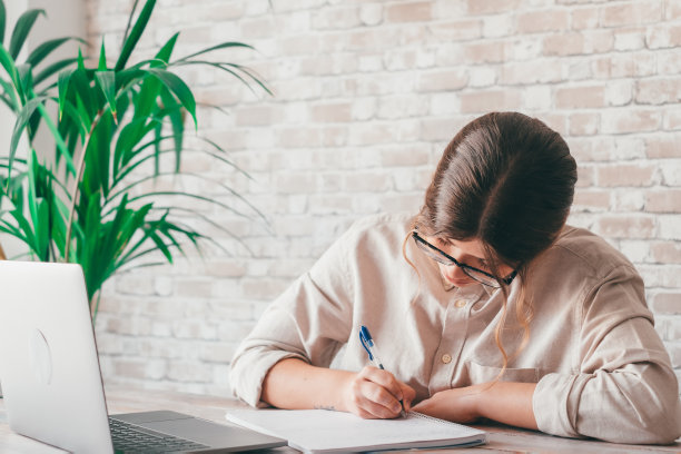 微笑的女人写笔记在笔记本电脑上看网络研讨会学习工作，年轻的学生学习计算机课程听力讲座培训翻译在线教师翻译班图片下载