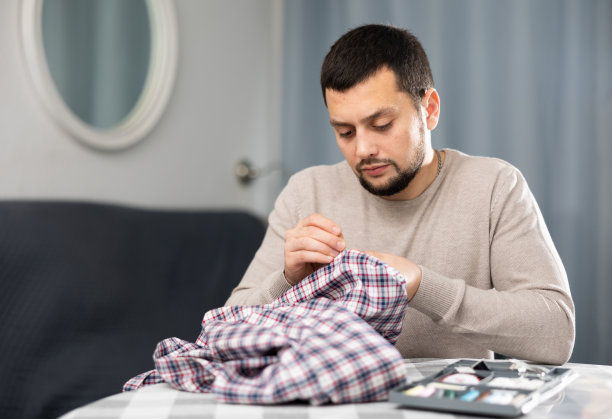 年轻人在家里的桌子上缝衬衫袖子上的扣子图片下载