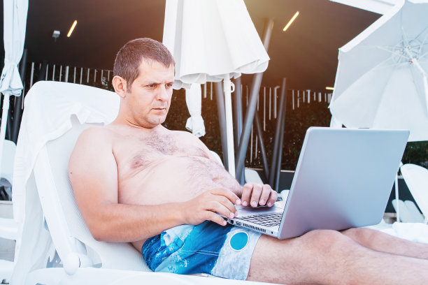 在笔记本电脑上工作的自由职业者，在海滩上打字。技术和旅行。在户外工作。自由的概念。一个度假的男人在泳池边用电脑工作。假期休息和工作。在假期远程工作。图片下载