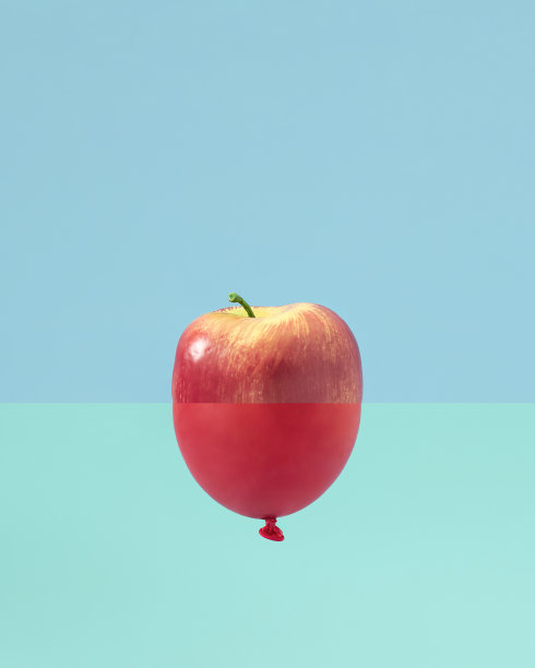 一边是半个苹果，另一边是红色气球的创意概念。新鲜多汁的水果在柔和的蓝色背景。图片下载