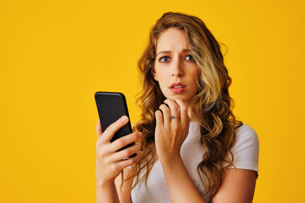 美丽的年轻女子的肖像与智能手机和手机隔离的黄色背景图片下载