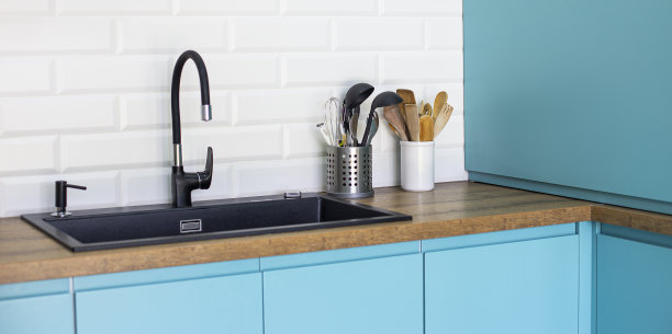 蓝色厨房的黑色水槽和水龙头，白色后挡板和木制台面图片下载