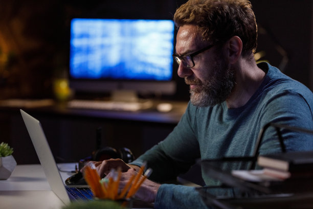 严肃的电脑程序员在工作到很晚的时候在笔记本电脑上输入代码的画像图片下载