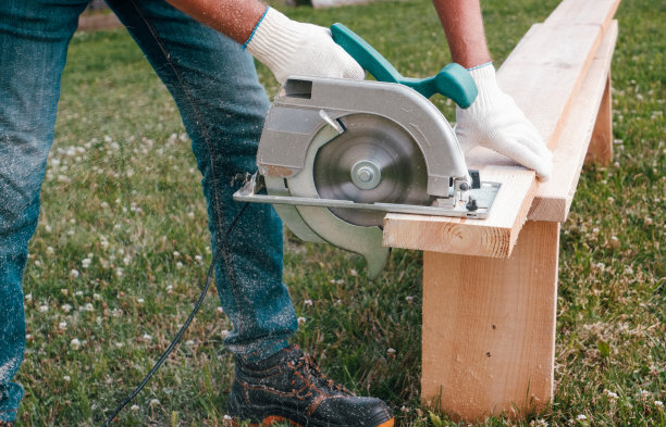 一名建筑工人用手持电锯在草坪上锯一块木板。在后院DIY。图片下载