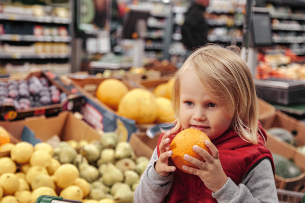 小女孩坐在食品、水果商店或超市的购物车里图片下载