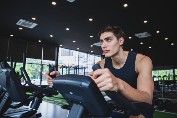 穿着运动服的年轻人在健身房的健身自行车上跑步训练图片下载