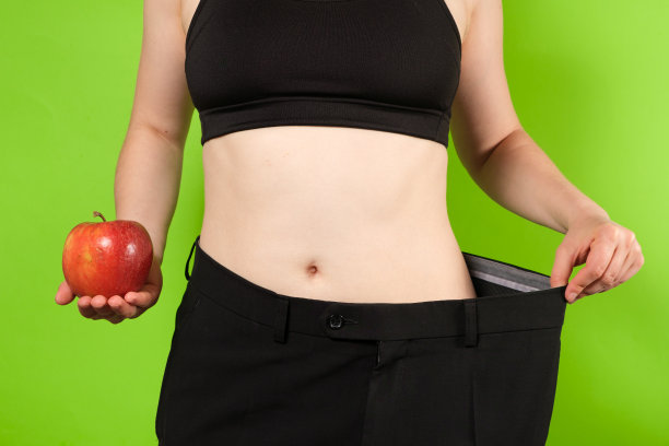 一个穿着大裤子的女人在绿色的背景上拿着一个苹果。图片下载