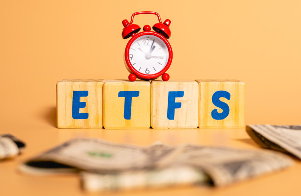 ETFS这个词来自交易所交易基金(etf)，用英语写在木制立方体上。闹钟和钞票的组合。经济和投资理念。素材图片