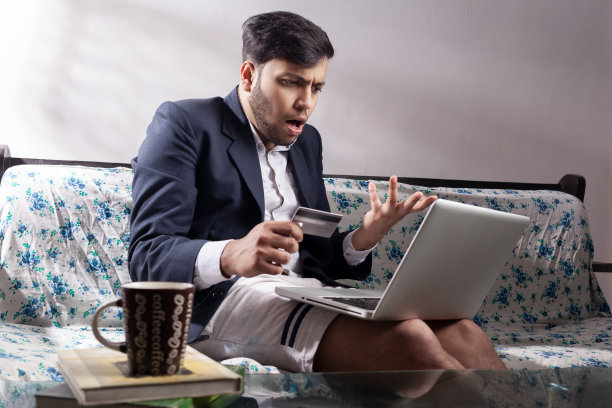 震惊的印度西装男在家里使用信用卡进行网上交易图片下载