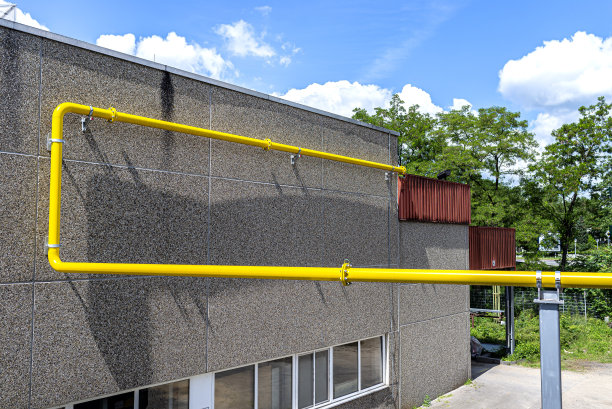 一条黄色的大煤气管道，沿着水泥墙和鹅卵石砌成的工厂墙壁。图片下载