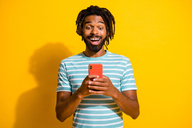 照片肖像兴奋的黑色皮肤的家伙拿着手机在两个手孤立在生动的黄色背景图片下载