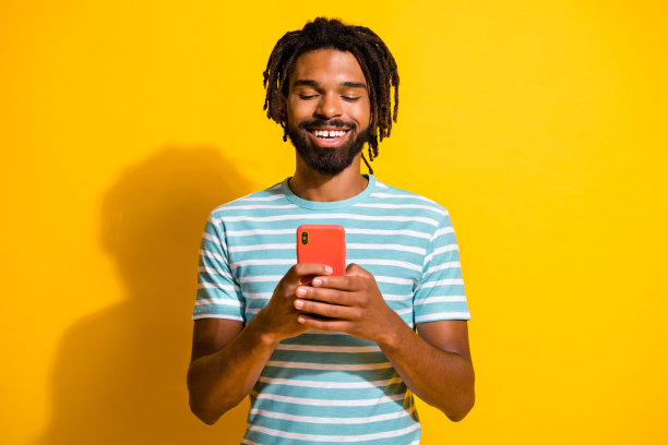 照片肖像微笑的黑色皮肤的家伙拿着手机在两个手孤立在生动的黄色背景图片下载