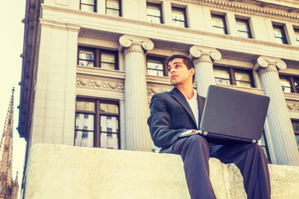 一个年轻人在纽约办公大楼外用笔记本电脑工作图片下载