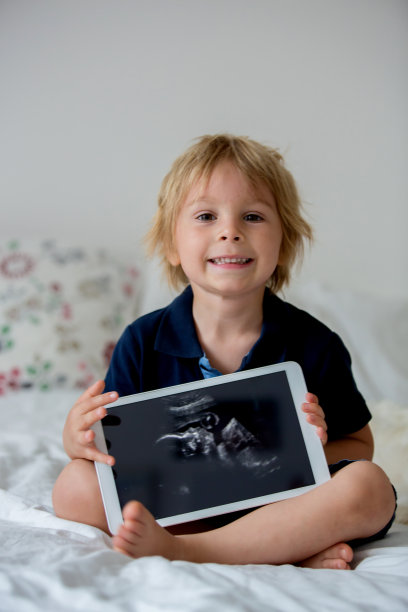 可爱的蹒跚学步的孩子，拿着他未出生的小妹妹的照片图片下载