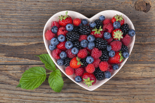 各色浆果放在白色质朴木桌的心形盘子里图片下载