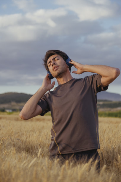 年轻英俊的男子在夏天的田野里听音乐图片下载