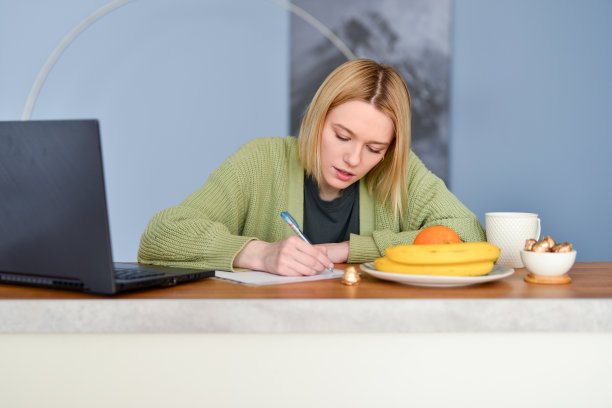 一名年轻女子在厨房的餐桌上做笔记图片下载