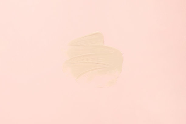 粉底霜的样品质地为脸部特写。在淡粉色的背景上涂抹粉底。图片下载