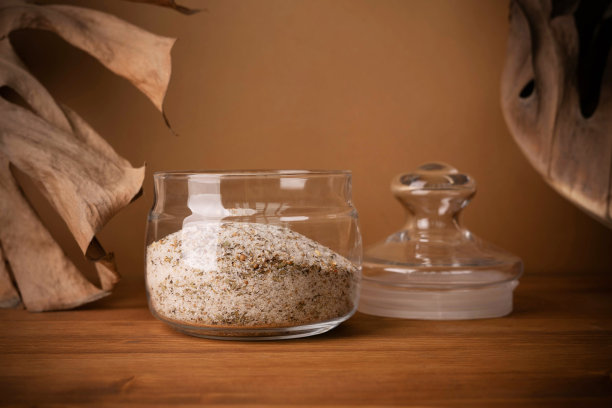 玻璃罐浴盐在米色背景与干燥的怪物叶子。图片下载