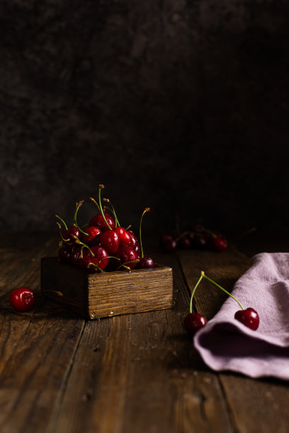 带水滴的樱桃装在一个木盒里，放在深棕色的木桌上。黑暗图片下载