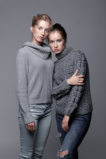 两个穿着灰色毛衣，灰色背景的年轻女人。美丽的女孩伸出双手拥抱。女性友谊的概念图片下载