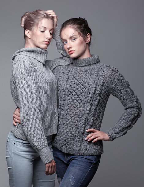 两个穿着灰色毛衣，灰色背景的年轻女人。美丽的女孩伸出双手拥抱。女性友谊的概念图片下载