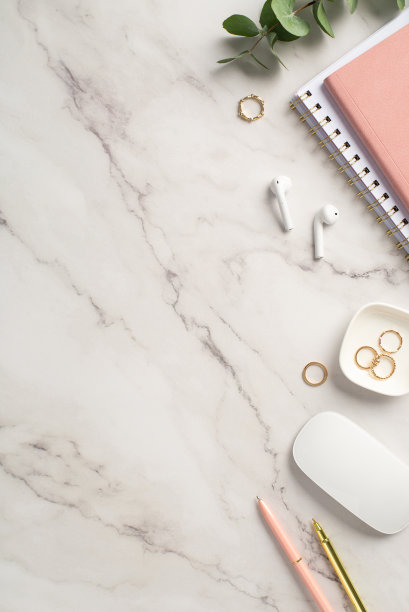 经营理念。俯视图垂直的工作空间的照片粉红色的记事本笔，金戒指，电脑鼠标，无线耳机和桉树在白色大理石背景图片下载