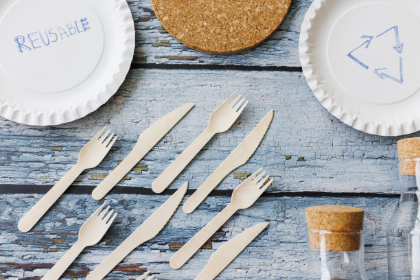 浅蓝色木制背景上的环保餐具平面组合。牛皮纸盘子和木制餐具。可回收的纸制品，零浪费的理念。有选择性的重点图片下载