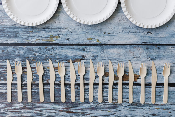 浅蓝色木制背景上的环保餐具平面组合。牛皮纸盘子和木制餐具。可回收的纸制品，零浪费的理念。有选择性的重点图片下载